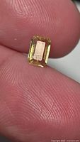Emerald-cut yellow sapphire on fingertip showing size and color