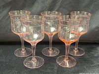 Front view of all five pink etched stemmed glasses standing in a group