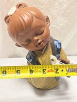 Front view of ceramic child figurine with measuring tape showing width