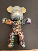Front view of multicolor paint-splatter bear figurine lying flat