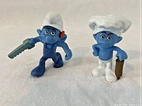 Handy Smurf and Baker Smurf side by side on white background