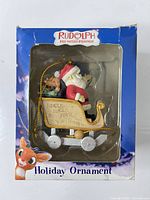 Front of boxed Rudolph ornament showing Santa in sleigh through window