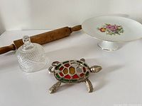 Group shot of cake stand, glass lid, turtle trivet and rolling pin