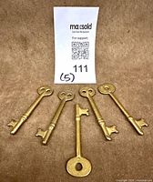 Five brass skeleton keys displayed on fabric background with MaxSold tag