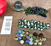 Group shot showing red cup, large shooter, assorted small marbles