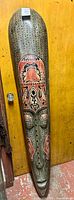 Full view of elongated carved wood mask with painted motifs