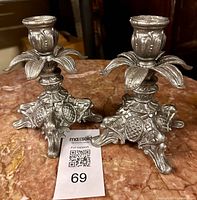 Pair of silver-tone ornate metal candlestick holders on marble surface