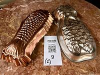 Copper fish mold and aluminum pineapple mold side-by-side on surface