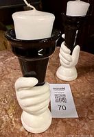 Two dolomite hand cone candleholders with white pillar candles on marble surface