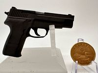 Left side view of miniature Sig Sauer P226 on stand beside Canadian loonie for scale