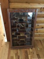 Front view of rosewood curio cabinet showing carved crest, glass front, mirrored back