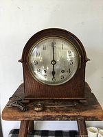 Front view of wooden mantel clock with dial, bezel, key and pendulum bob on table