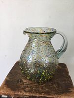 Full view of multicolour blown glass pitcher on stool