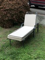 Full view of metal outdoor chaise lounge with cushion on grass