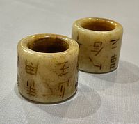 Two cylindrical jade thumb rings showing carved characters and coloration