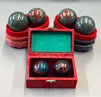 Three sets of Baoding balls displayed, one box open, two oval cases used as stands