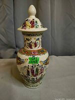 Front view showing figures, bird motif, lid finial