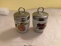 Front view of both egg coddlers showing fruit motifs and lids