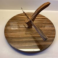 Top view of round wooden cheeseboard with glass surface, arched handle, and knife
