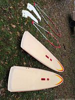 Two BIC windsurf boards bottom side up on grass with two booms and two daggerboards