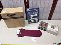 All four items: boxed HoMedics massager, sealed Proctor Silex travel iron, boxed metal-frame photo album, burgundy Built neoprene sleeve