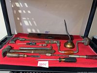 All hand tools laid out on red surface: brace, bits, level, oil can, hammers, chisels, screwdrivers, awl, file