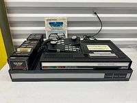 Overall lot showing console, two controllers, ten cartridges, manual, storage tray