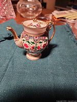 Front view of porcelain miniature teapot showing floral design, gold handle and spout