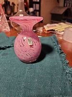 Front view of pink swirling Mina Glass bud vase with label visible