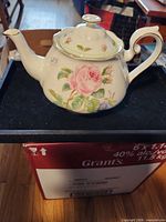 Left side view of teapot showing rose design and gold-trimmed spout, handle and lid