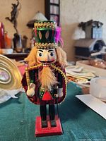 Front view of wooden nutcracker showing cape, sword, wand, hat and base
