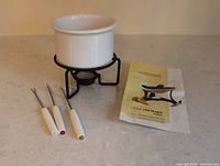 Complete fondue set laid out: pot on stand, three forks, instruction leaflet