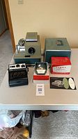 Lot overview showing projector, case lid, slide viewer, Kodak camera, boxes and leaflet