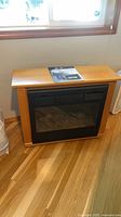 Frontal view of electric fireplace showing mantel, vent, glass front, faux logs