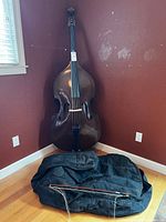 Full view of double bass standing upright with case and bow on floor