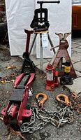Group shot of pipe vise on tripod, floor jack, bottle jack, two jack stands, tow chain with hooks