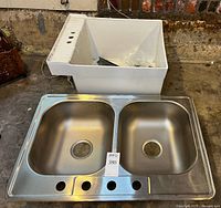 Double bowl stainless steel sink and white utility tub side by side on floor