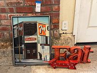 Overall view of framed poster leaning against wall beside metal “EAT” sign