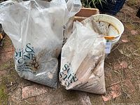 Two plastic bags of gravel and white bucket beside terracotta planter on brick ground