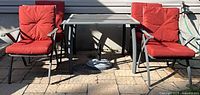 Full view of table, four chairs with red cushions, umbrella stand underneath