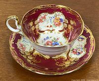Teacup on saucer showing burgundy glaze, gold scrollwork and floral panels