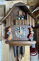 Front view of wooden chalet cuckoo clock showing dial, side figures, dancers, weights