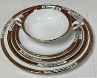 Stack of plates in various sizes with handled soup bowl on top showing pattern and gold edging