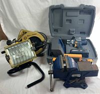 Group shot of all four tools: circular saw, halogen light, cordless drill set in case, bench vise