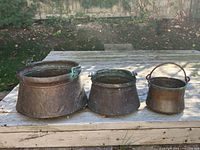 Three copper pots side by side on deck, showing size comparison and patina