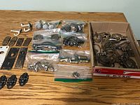 Overview of assorted hardware laid out on table, including bagged items and box of brass pulls