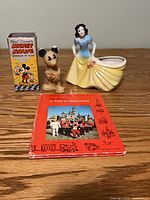 Front view of all three items: Mickey Mouse soap with box, Snow White planter, Disneyland book