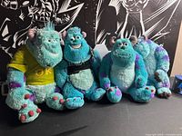 Four Sulley plush toys lined on table, two with shirts