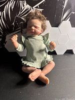 Front view of realistic baby doll seated, showing facial features and outfit