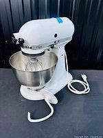 Full view of white stand mixer with stainless bowl and wire whisk attached